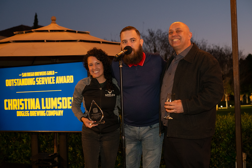 San Diego Brewers Guild representatives Erik Fowler (middle) and Jake Nunes present the first-annual Outstanding Service Award to Christina Lumsden from Dogleg Brewing