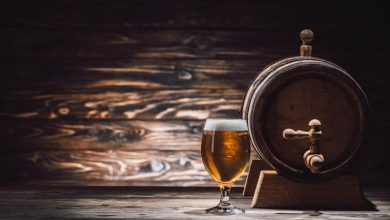 A glass of expensive beer sits beside a wooden barrel on a rustic table