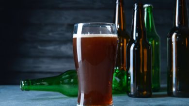 A pint glass of homebrewed beer surrounded by empty bottles, ready for bottling