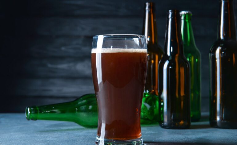 A pint glass of homebrewed beer surrounded by empty bottles, ready for bottling