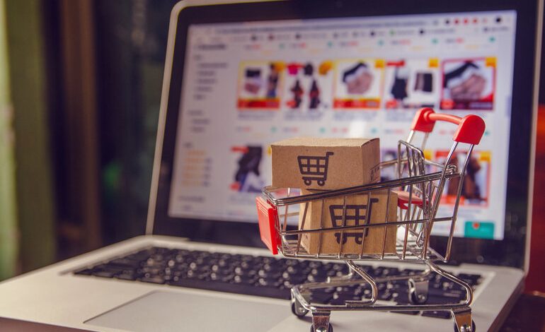 A miniature shopping cart with boxes placed on a laptop displaying a private-level e-commerce site