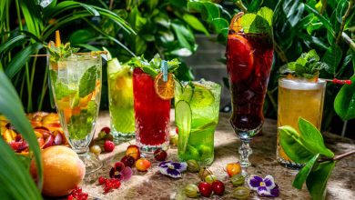 Botanical cocktails with colorful garnishes on a rustic table surrounded by lush greenery