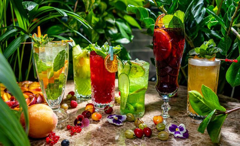 Botanical cocktails with colorful garnishes on a rustic table surrounded by lush greenery