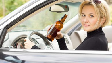 Woman holding a beer bottle while seated in the driver's seat of a car, facing a potential DUI charge