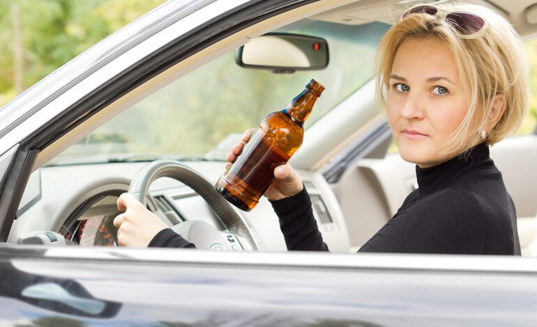 Woman holding a beer bottle while seated in the driver's seat of a car, facing a potential DUI charge