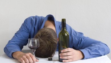 A college student with his head down on a table next to a beer bottle and glass