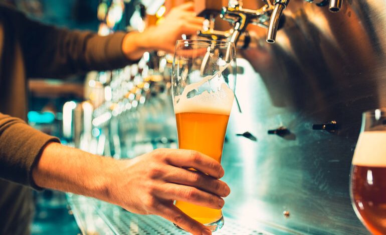 A bartender pouring a hazy craft beer from a tap at a San Diego brewery