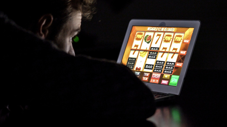 A man in front of an online casino slot machine on a laptop