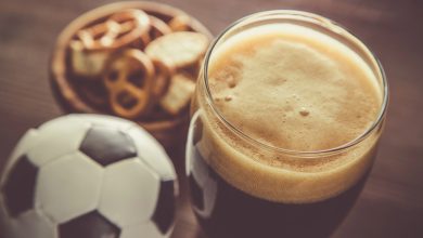 Glass of beer with bowl of snacks and football