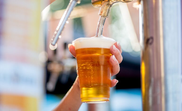 A traveller pouring a glass of golden craft beer from a tap at an outdoor San Diego brewery