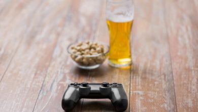 Glass of craft beer, game controller, and bowl of snacks on rustic wooden table