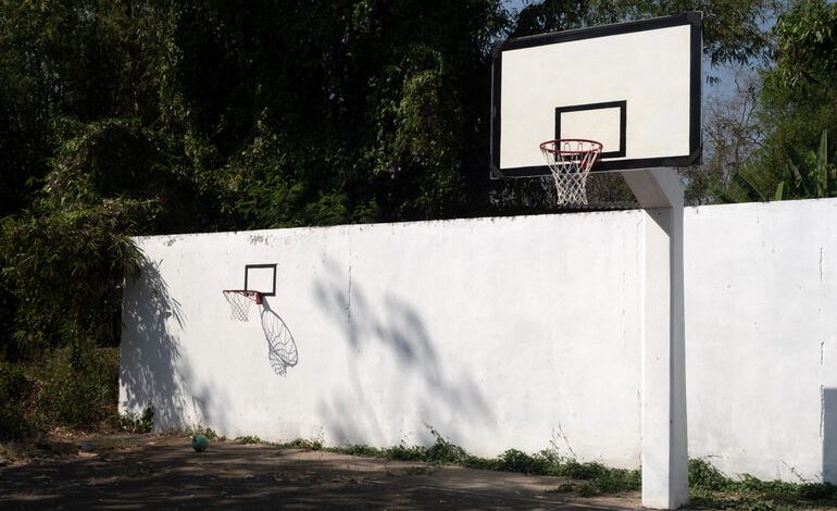 Two outdoor basketball hoops stand on a worn court beside a white wall in Zambia