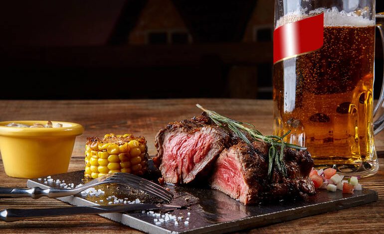 Juicy medium-rare steak served with grilled corn and a frosty mug of craft beer