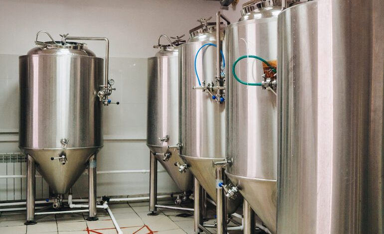 Row of bar stools facing fermentation tanks inside a modern San Diego brewery