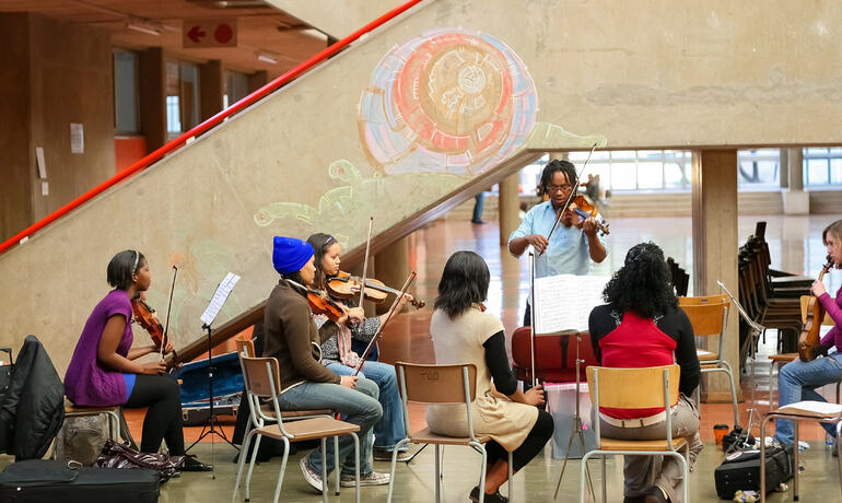 Students participate in a community violin lesson led by an instructor inside a public space
