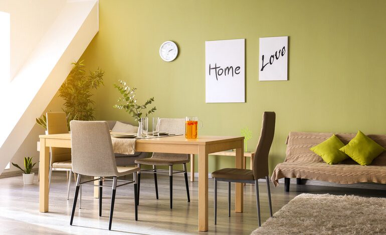 Modern dining and living space with green accent wall, minimal wooden furniture, indoor plants, and stylish decor that blends comfort with low-maintenance design