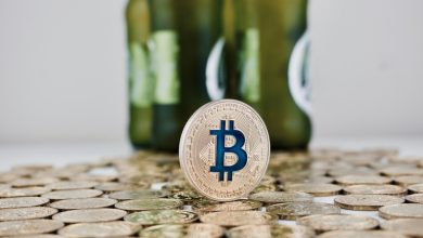 Bitcoin token standing on a pile of coins with blurred beer bottles in the background