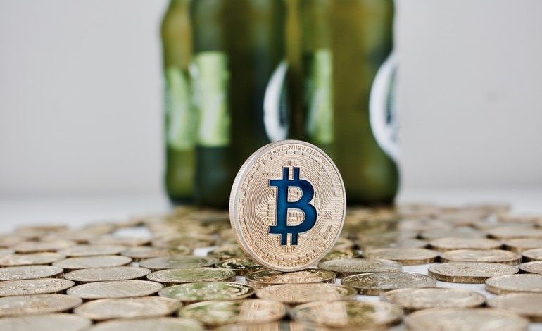 Bitcoin token standing on a pile of coins with blurred beer bottles in the background
