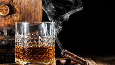 A glass of whiskey with smoke rising from cigars beside a wooden barrel