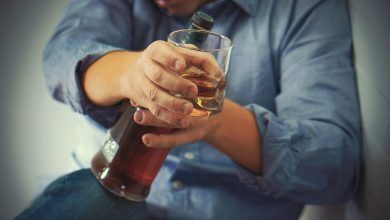 A distressed person sits with a bottle of alcohol and a glass