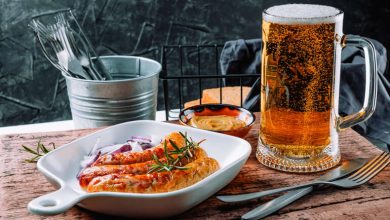 A glass of craft beer served with grilled sausages, onions, and dipping sauces in San Diego