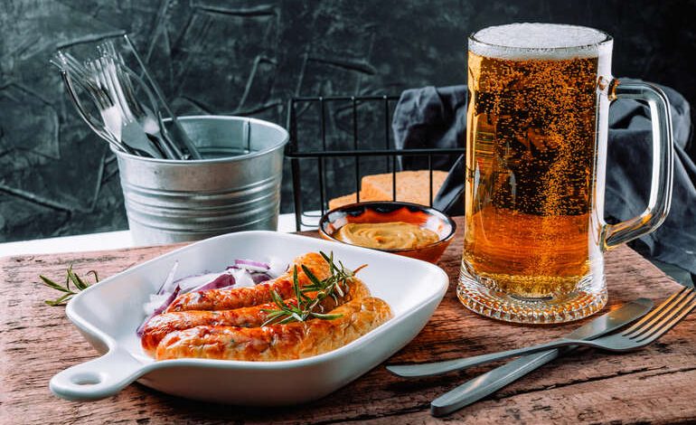 A glass of craft beer served with grilled sausages, onions, and dipping sauces in San Diego