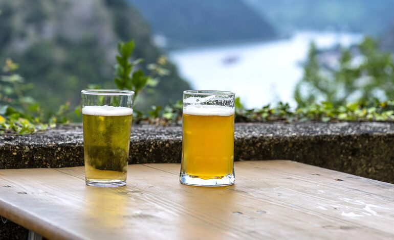 Two glasses of beer on a wooden table overlooking a scenic mountain and river outside the USA