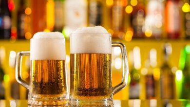 Two frothy pints of craft beer on a bar counter with colorful bottles in the background, perfect for enjoying while playing slots