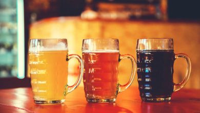 Three mugs of craft beer in varying colors, from light to dark, on a bar counter in a cozy, dimly lit San Diego taproom, perfect for a late-night drink