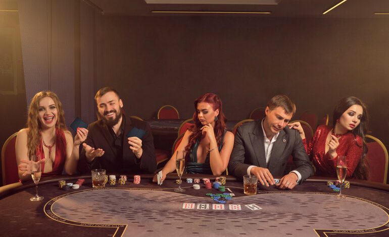 Group of stylish people playing poker at a casino table, enjoying drinks and the thrill of a live dealer game experience
