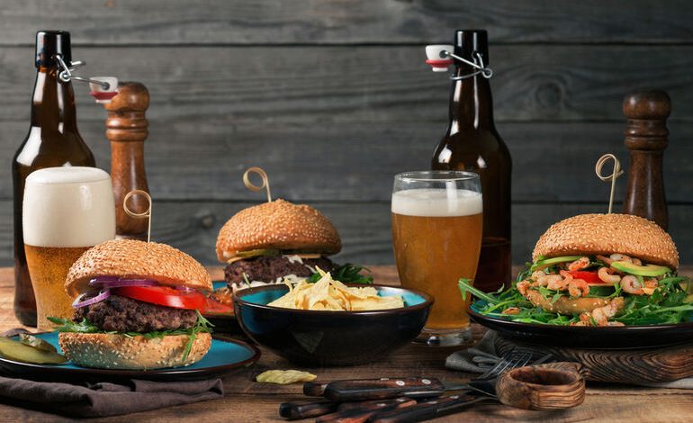 Gourmet burgers, chips, and craft beers on a wooden table for a cannabis beer and food pairing guide
