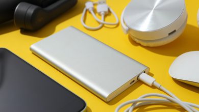 A slim silver power bank charging a device, surrounded by gadgets like headphones, a smartphone, and cables