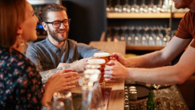 A friendly bartender hands craft beers to a smiling couple at the bar