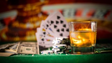 A glass of whiskey, poker chips, playing cards, and cash on a casino table.