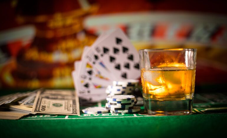 A glass of whiskey, poker chips, playing cards, and cash on a casino table.