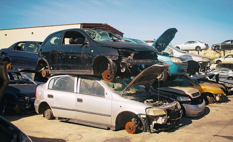Junkyard cars stacked for parts comparison to online auto auctions.