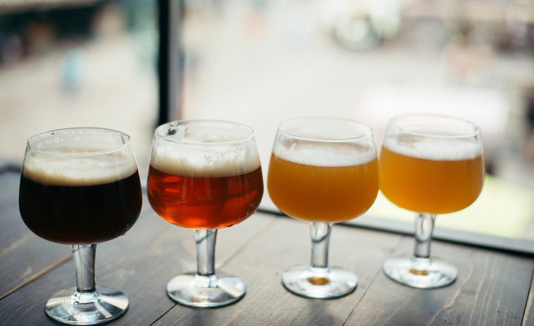 Different types of beer served in clear glasses on a wooden surface.