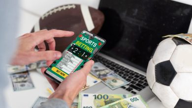 Person placing bets on a mobile sports betting app with a football, soccer ball, laptop, and cash on the table