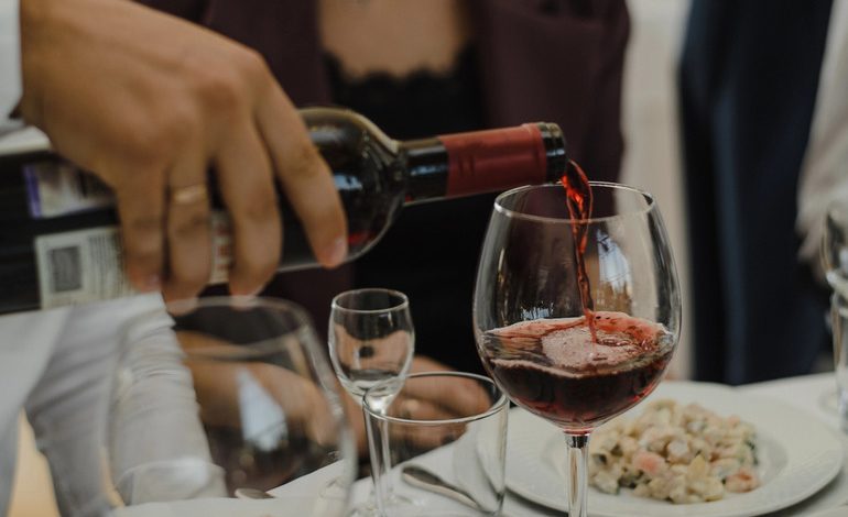 A person pouring red wine into a glass at a dinner party