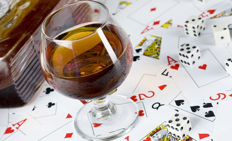 Glass of alcohol with playing cards and dice symbolizing the influence of drinking on casino gaming decisions.