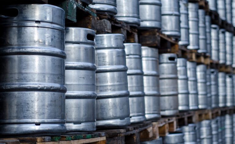 Rows of metal beer kegs stacked on wooden pallets in a storage area.