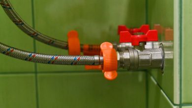Close-up of a braided steel drain hose connected to a wall valve with red and orange knobs, demonstrating proactive drain care setup for brewers.