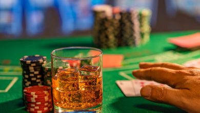 A glass of beer with ice on a casino table beside poker chips and playing cards.