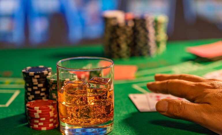 A glass of beer with ice on a casino table beside poker chips and playing cards.