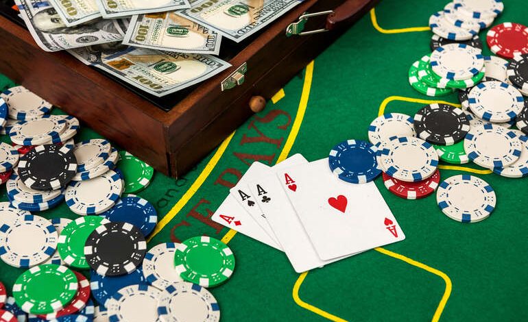 Poker table with playing cards showing four aces, surrounded by casino chips and stacks of hundred-dollar bills.
