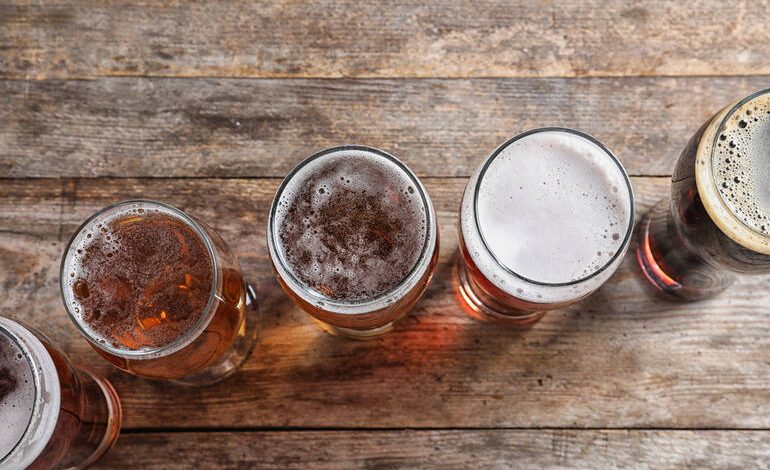A top-down view of five different craft beers in glasses on a rustic wooden table