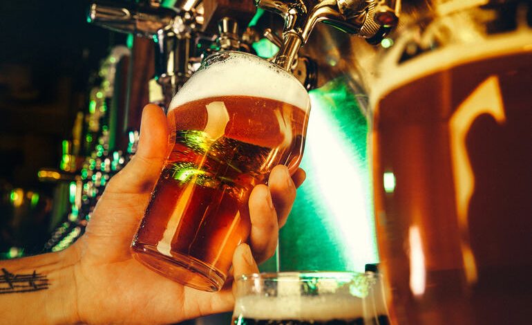 A beer lover is pouring craft beer from a tap into a glass at a brewery with warm lighting