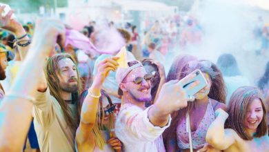 A Group of friends covered in colorful powder, taking a selfie, and celebrating at an outdoor festival, enjoying vibrant energy and summer vibes.