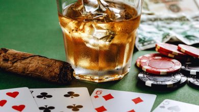 Glass of beer with ice, cigar, poker chips, money, and playing cards representing the connection between gambling and drinking in casinos.