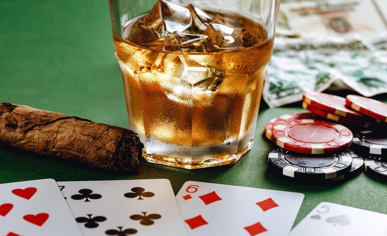 Glass of beer with ice, cigar, poker chips, money, and playing cards representing the connection between gambling and drinking in casinos.